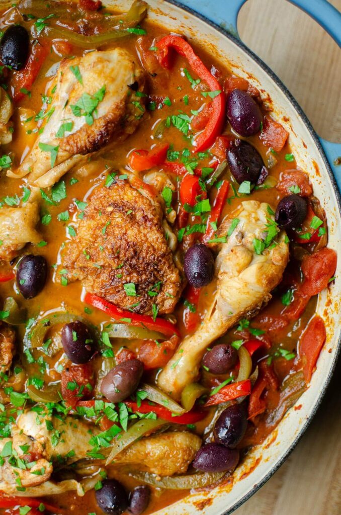 Cooked chicken with peppers and olives and parsley sprinkled over top in a blue braising dish.